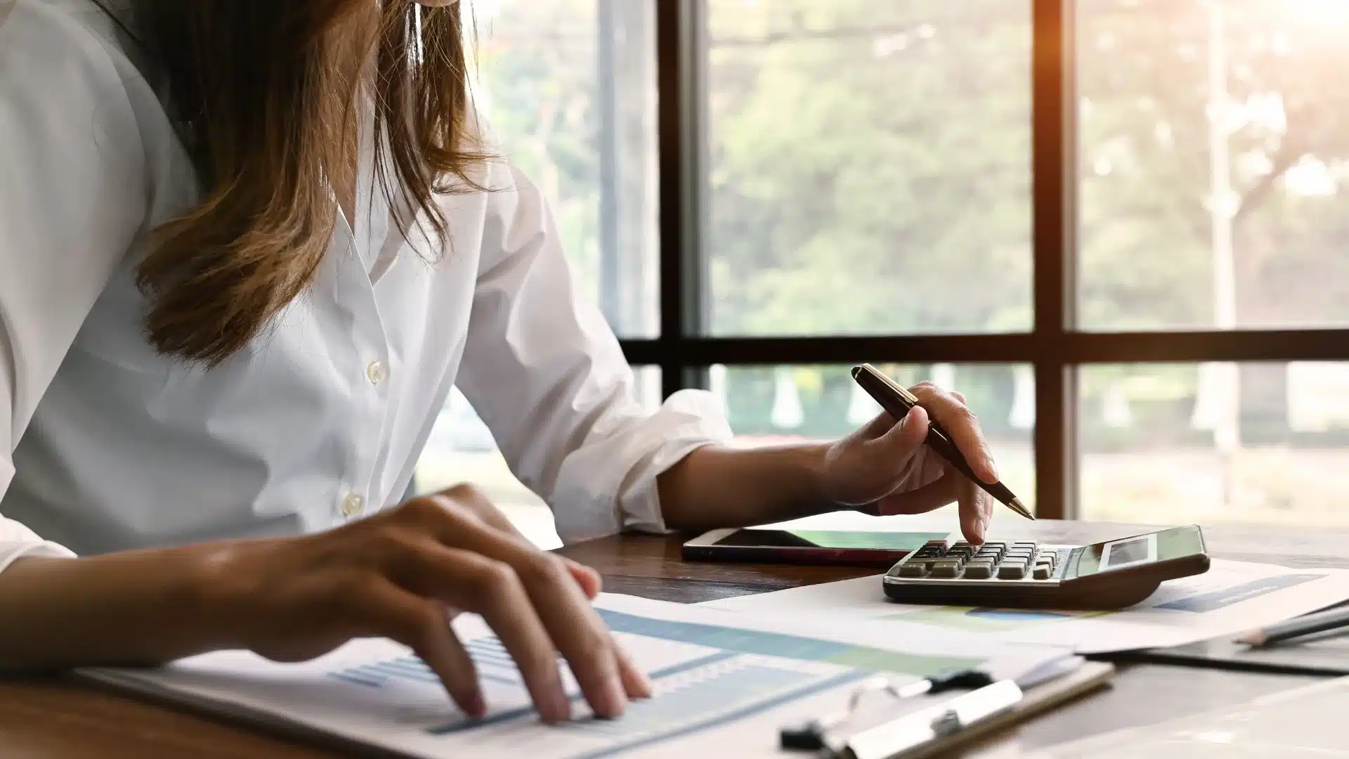 Finance professional reviewing reports and using a calculator at a desk, representing the process of evaluating contract-to-hire finance positions and making strategic career decisions.